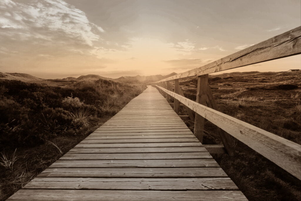 Boardwalk across grassy fields at sunset.