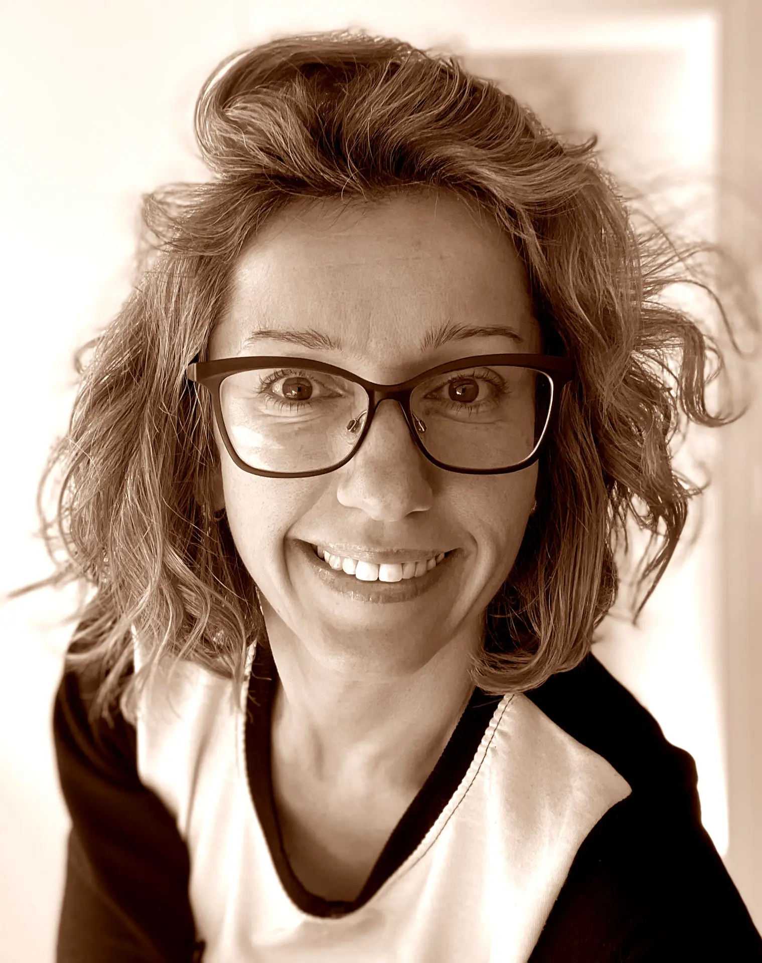 Female yoga teacher with prescription sunglasses, she has brown hair shoulder length and wears a dark t-shirt.